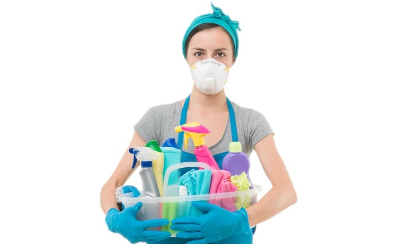 A woman is standing with a basket full of cleaning supplies