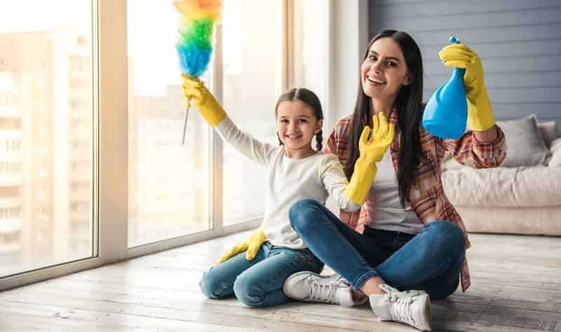 young mother and her daughter sitting on the floor and holding duster and spray bottle