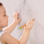 A child using pencil on wall inside a room