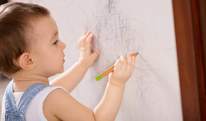 A child using pencil on wall inside a room