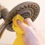 A hand with yellow cloth scrubbing shower head