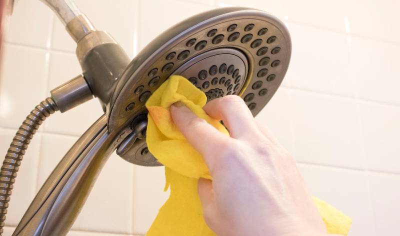 A hand with yellow cloth scrubbing shower head