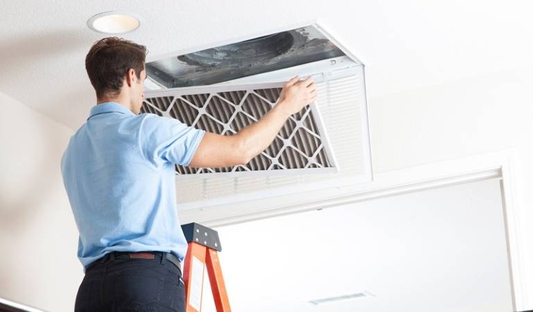 Man in blue shirt black pant opening air duct inside a room