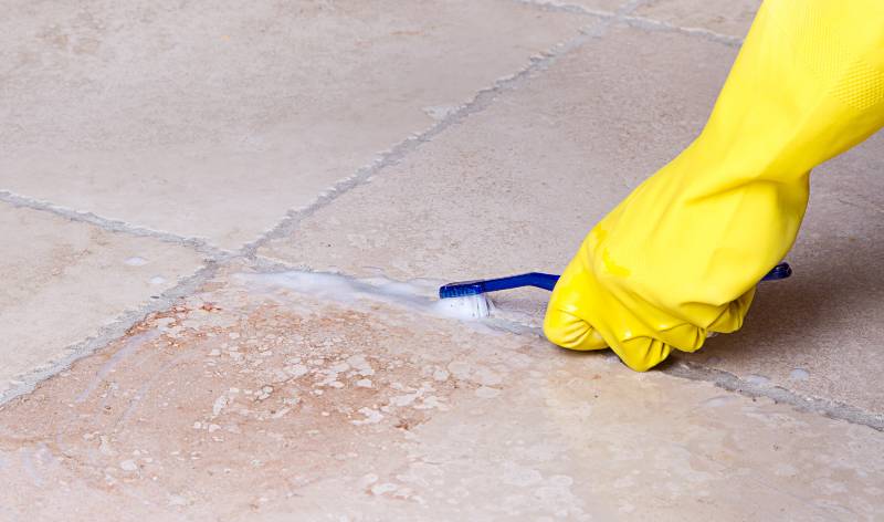 Hand in yellow gloves holding a brush scrubbing grout
