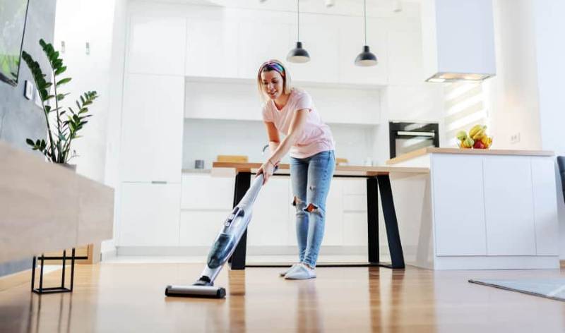 Woman in pink t-shirt and blue jeans vacuuming floor inside a room