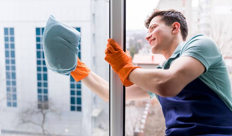 Man in in orange gloves washing window.