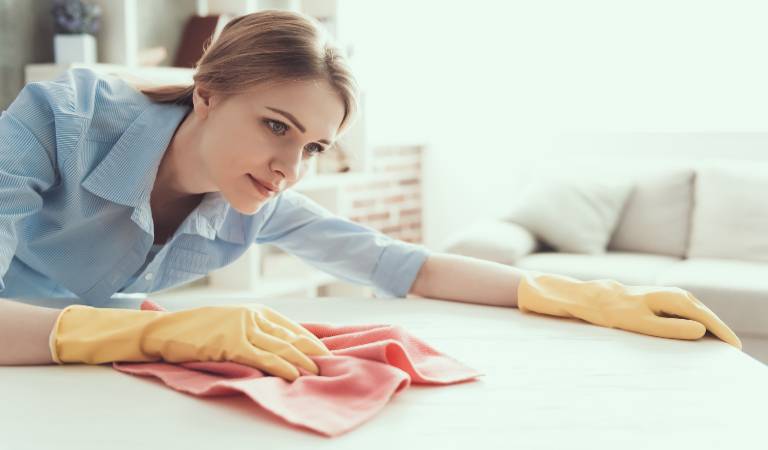 Woman in yellow gloves scrubbing table with pink cloth