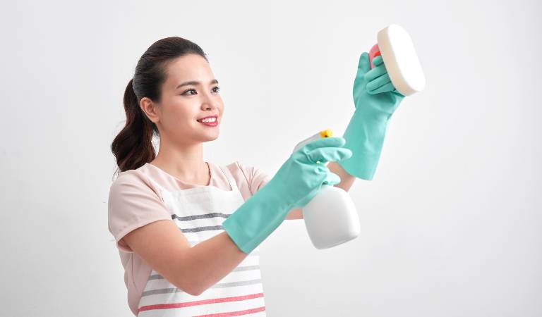 Woman in green gloves holding a white bottle in her hand spraying inside a room