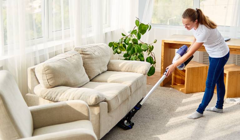 Woman in white top blue jeans vacuuming floor inside a living room