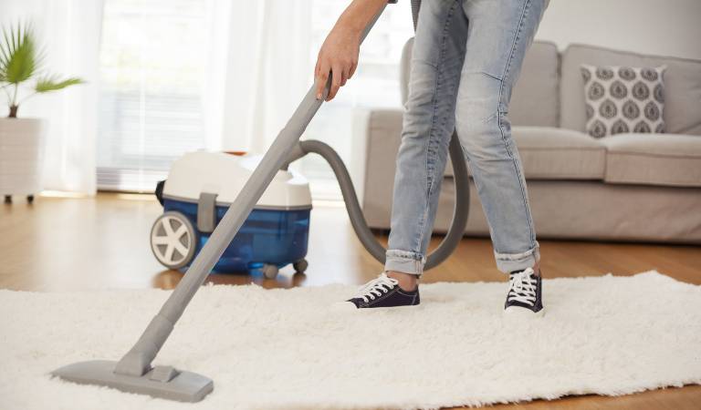 Woman vacuuming carpet with vacuum cleaner inside a living room.