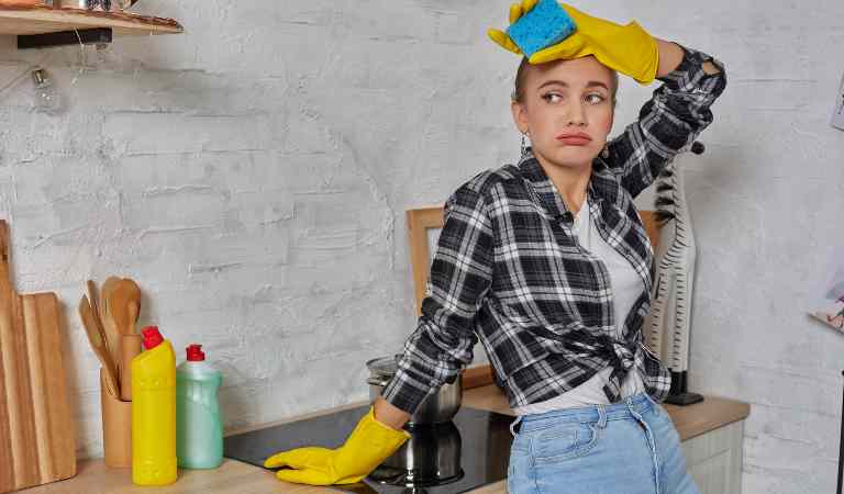 A lady in check shirt, blue jeans and yellow glove put her hand of her head and looking disturbed.