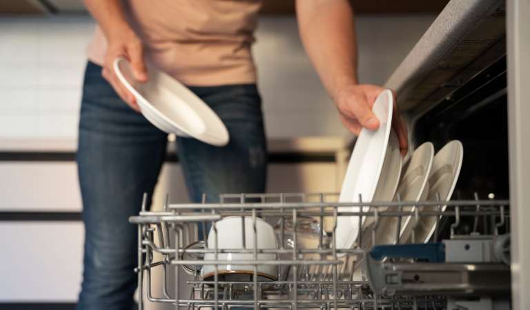 Woman in yellow top and blue jeans putting plates in dishwasher