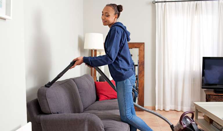 Woman is vacuuming her sofa inside her living room