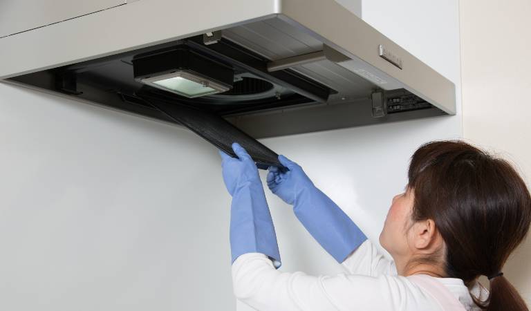 Woman in white shirt and blue glove cleaning air ducts inside kitchen