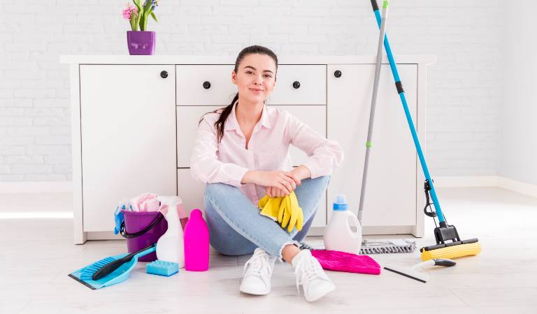 Woman sitting on the floor with cleaning tools, bottles, cloth, cleaning stick etc.