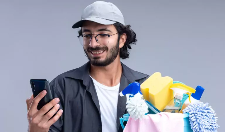 young man with some cleaning supplies and a phone in hand