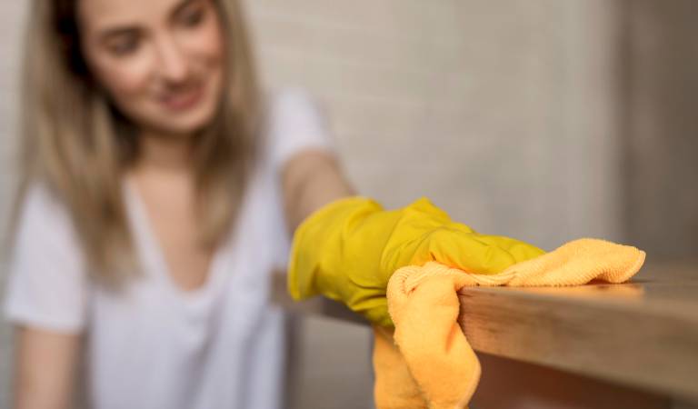 Woman in white top and yellow glove cleaning a table with a microfiber cloth