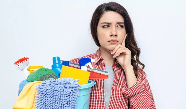 Woman looking worried and holding a bucket full of cleaning supplies