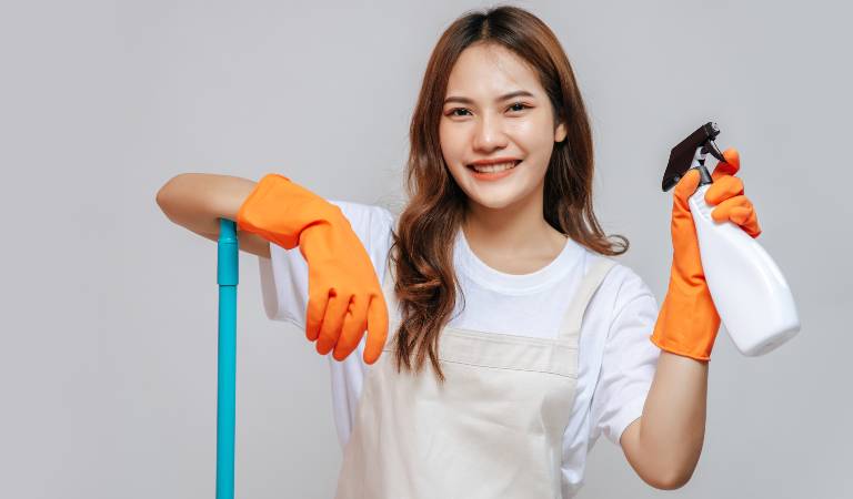 Smiling woman in white top and orange gloves holding a white bottle in her hand.