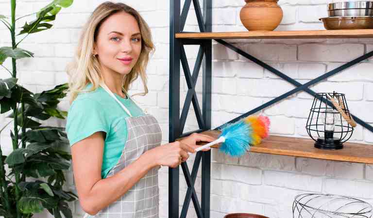 Woman in blue dress holding a duster in her hand and looking in front.