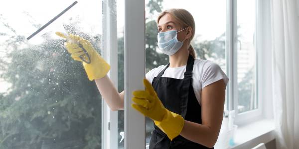 Professional cleaner in mask and yellow glove cleaning window.