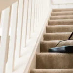 A person is cleaning stair carpets with the help of vacuum cleaner.
