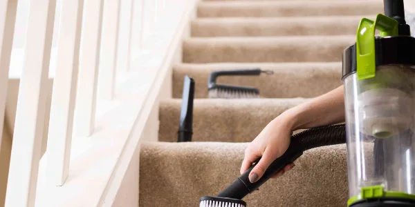 Hand of a woman holding a steam cleaner and cleaning stair carpets.