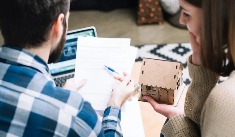 Man in blue check shirt reading a paper and holding a pen in his hand. Woman holding a house in her hand.