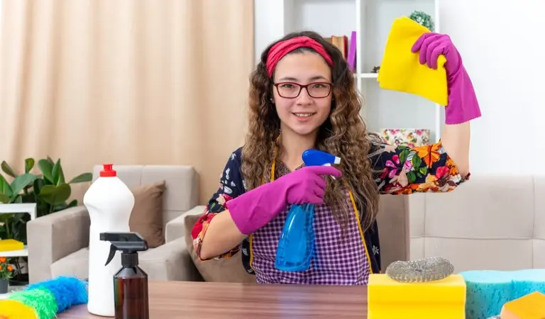 Woman in pink gloves holding a blue bottle and yellow cloth in her hand