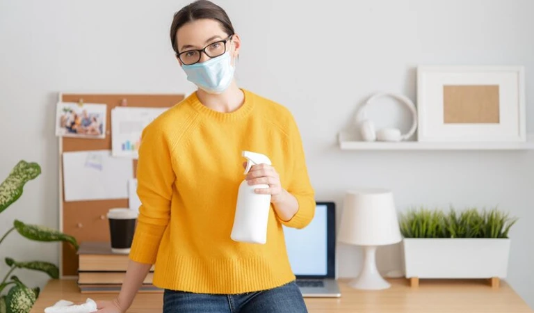 Woman in yellow top and a mask holding a white bottle in her hand