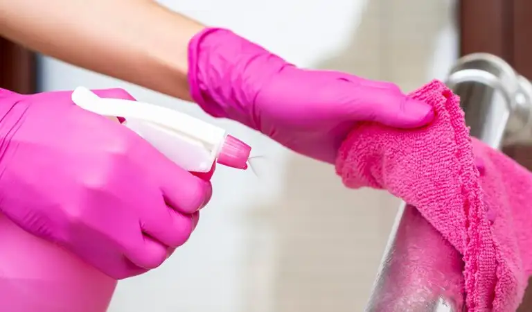 Hand of a woman in pink gloves cleaning steel with a cloth.