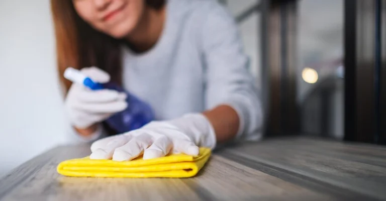 Lady is cleaning a table with a yellow cloth.