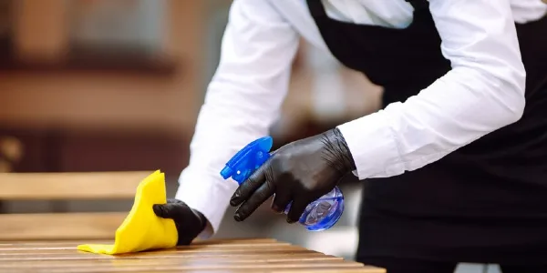 Professional cleaner in white-black dress cleaning a table with a yellow cloth.