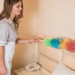 Happy female maid using duster to clean the wall of room