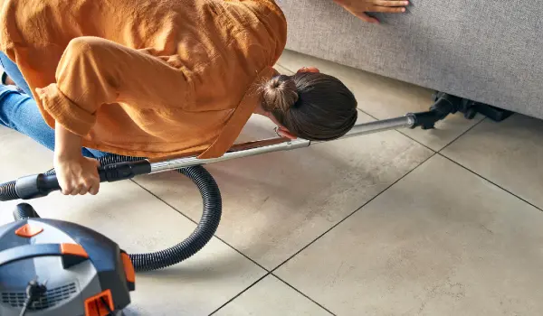 Woman vacuum cleaning under sofa in living room for housekeeping hygiene maintenance home