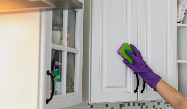 Hand in a purple rubber glove cleaning white kitchen cabinet
