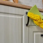 Hand in a purple rubber glove cleaning white kitchen cabinet