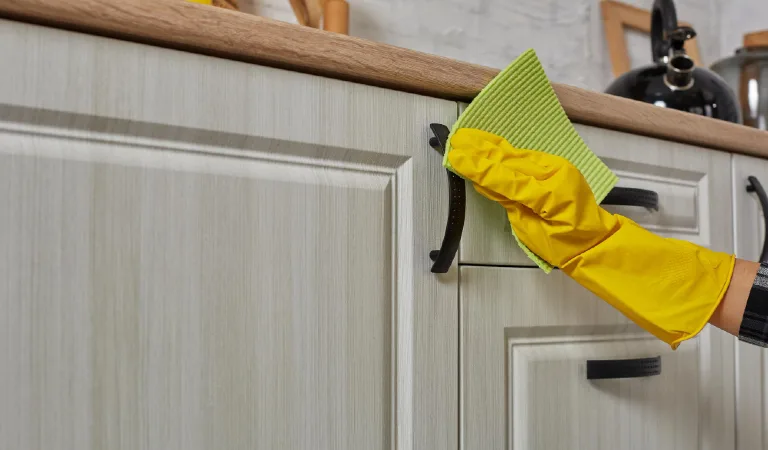 Hand in a purple rubber glove cleaning white kitchen cabinet