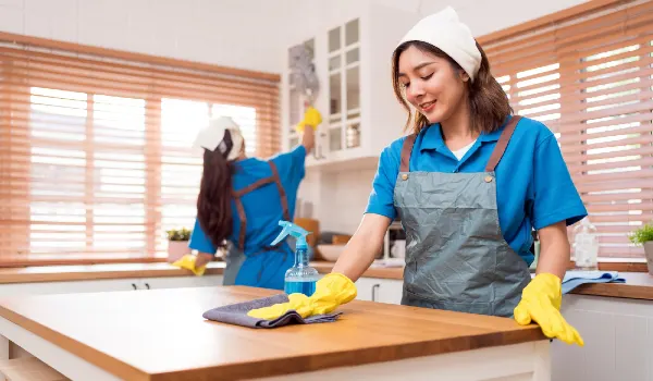 Professional asian woman cleaning service wearing yellow rubber gloves using rag to wipe with spray
