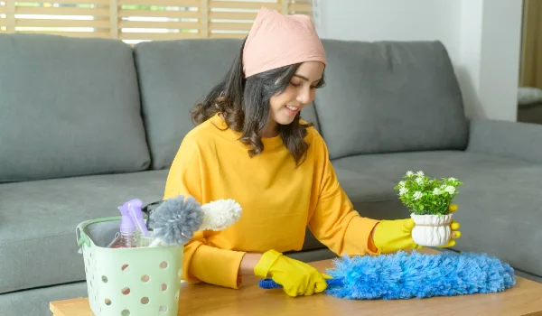 Young happy woman wearing yellow gloves and dusting the table in living room