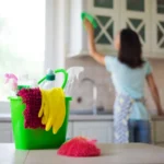 Happy beautiful young woman in yellow gloves is cleaning kitchen with special equipment and spray