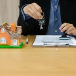 Midsection of businessman holding house key by papers on office desk