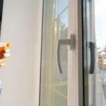 Woman manually washes window of house with a rag with spray cleaner