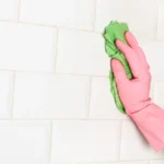 Man cleaning a wall of white subway tiles with a sponge cloth