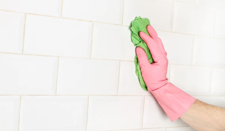 Man cleaning a wall of white subway tiles with a sponge cloth